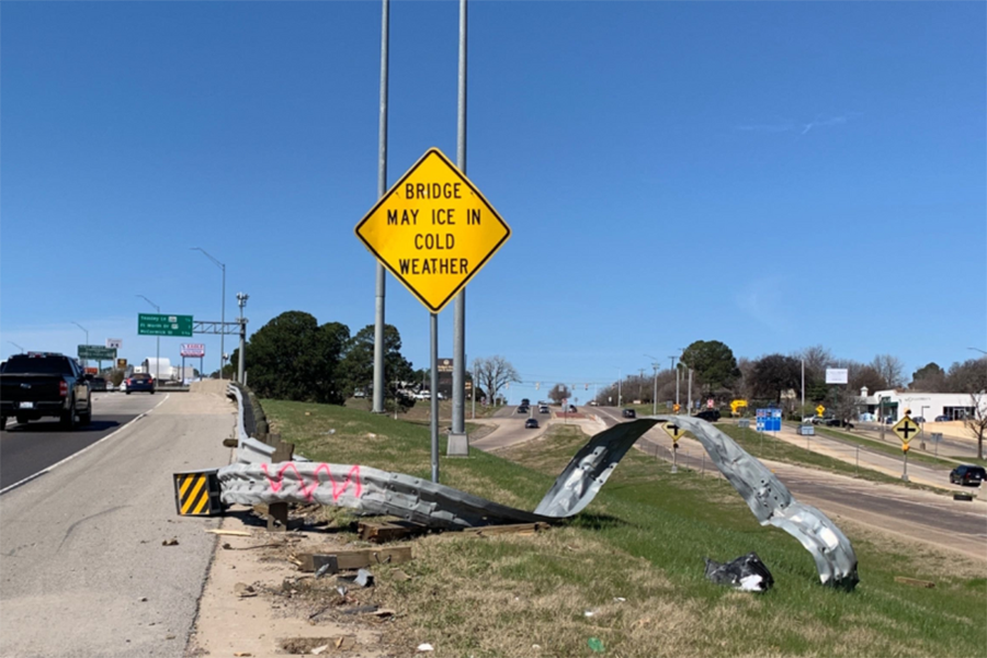 Twisted, damage guard rail on side of road approaching bridge